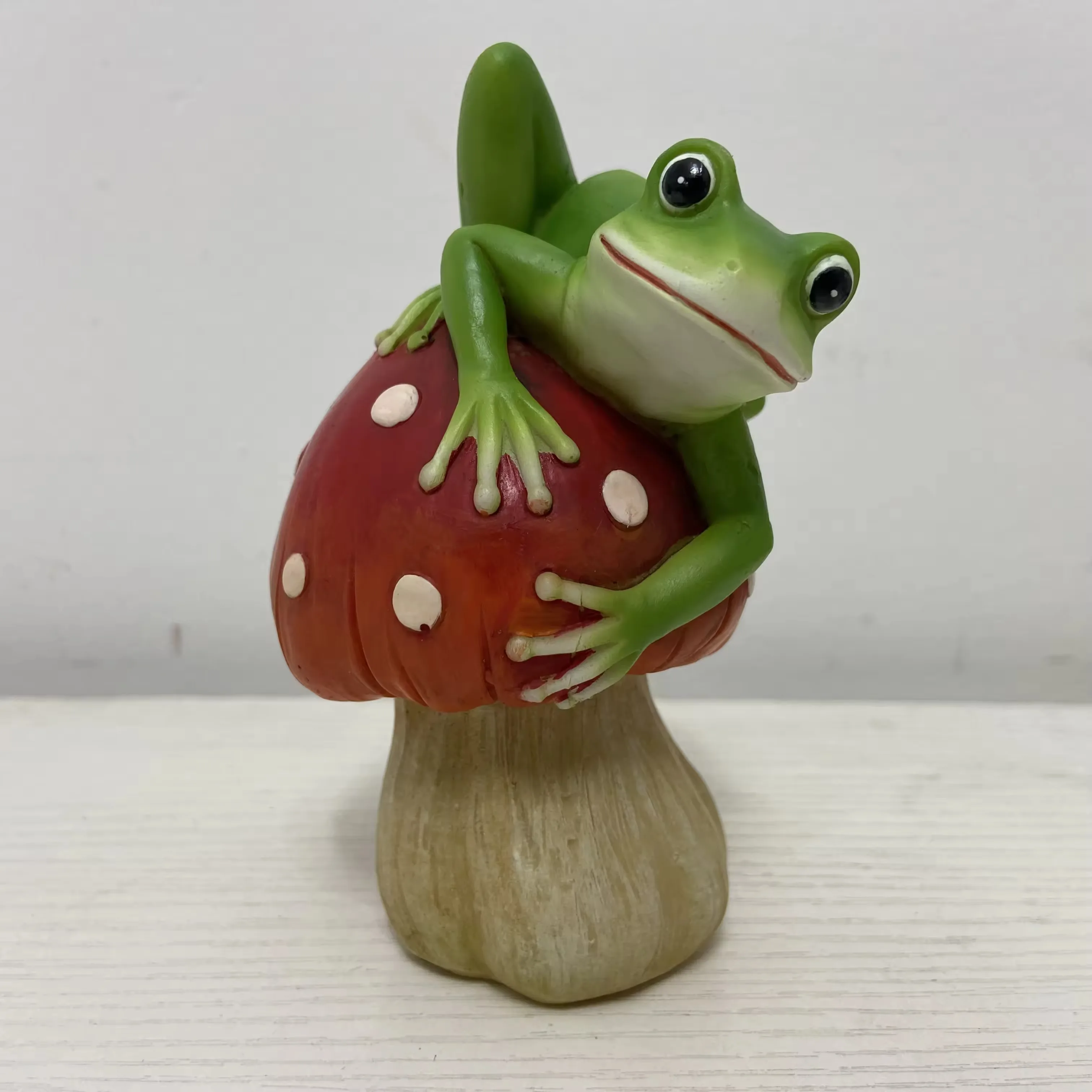 Mini figurine de rana en resina abrazando un hongo rojo con motas para adorno artistico de mesa y regalos corporativos