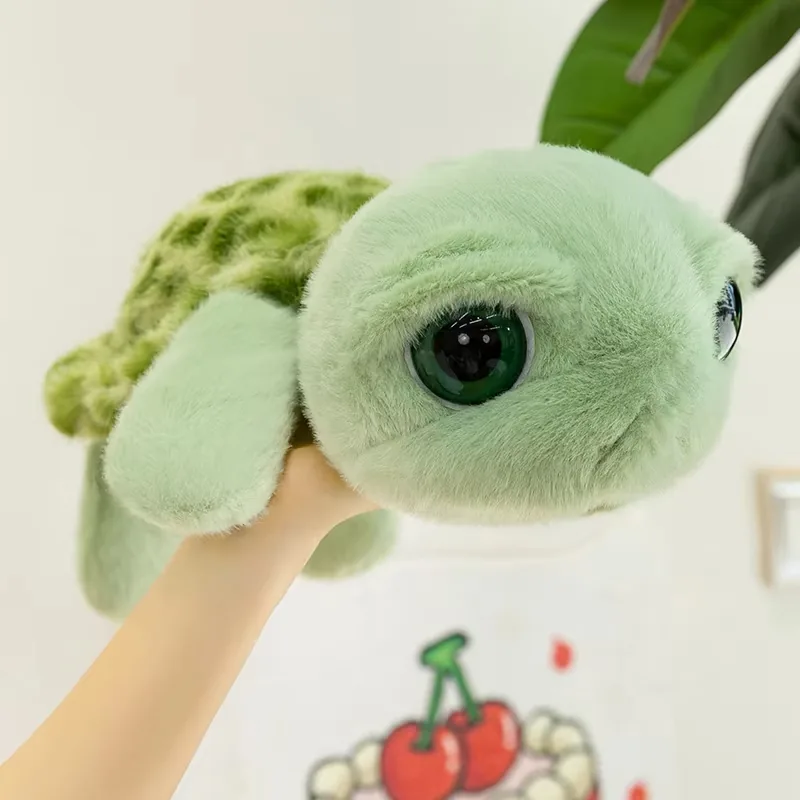 Peluche de tortuga de ojos grandes sostenido con una mano para mostrar el tamaño y la forma redondeada de tortuga marina