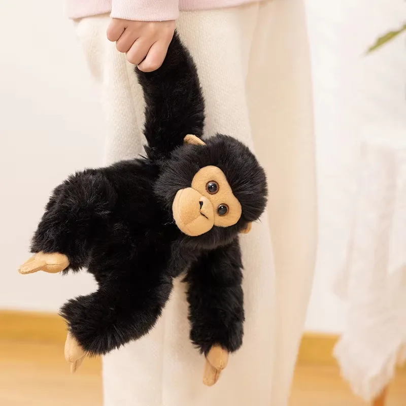 Peluche de chimpancé negro sostenido por un brazo para mostrar un cuerpo flexible y un tamaño fácil de llevar