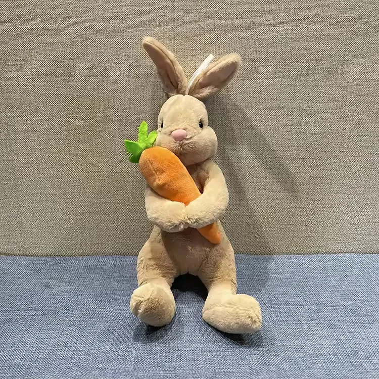 Peluche de conejo beige abrazando una zanahoria de gran tamaño con orejas largas erguidas