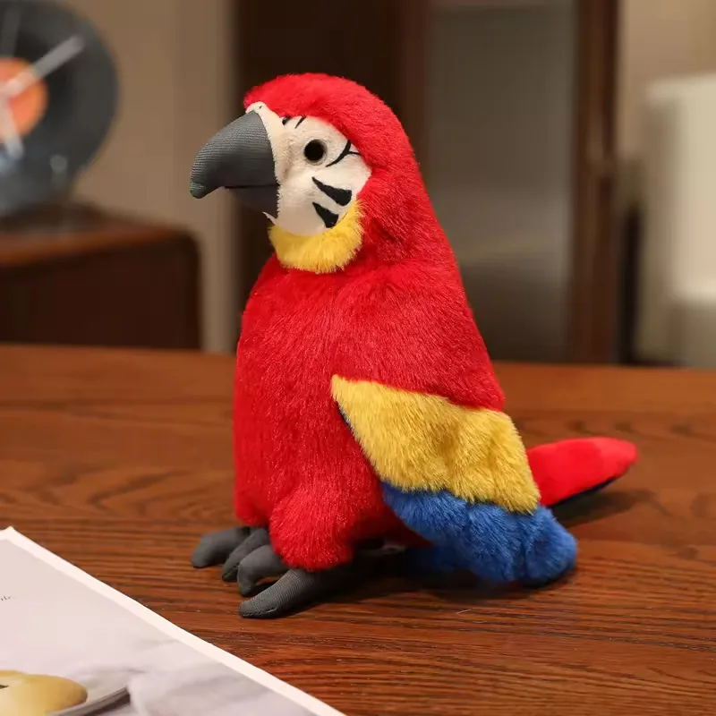 Loro de peluche rojo escarlata con alas amarillas y azules, posado erguido sobre una mesa