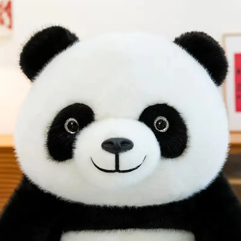 Primer plano de la cara del peluche de panda con manchas negras en los ojos, hocico redondeado y bordado sonriente