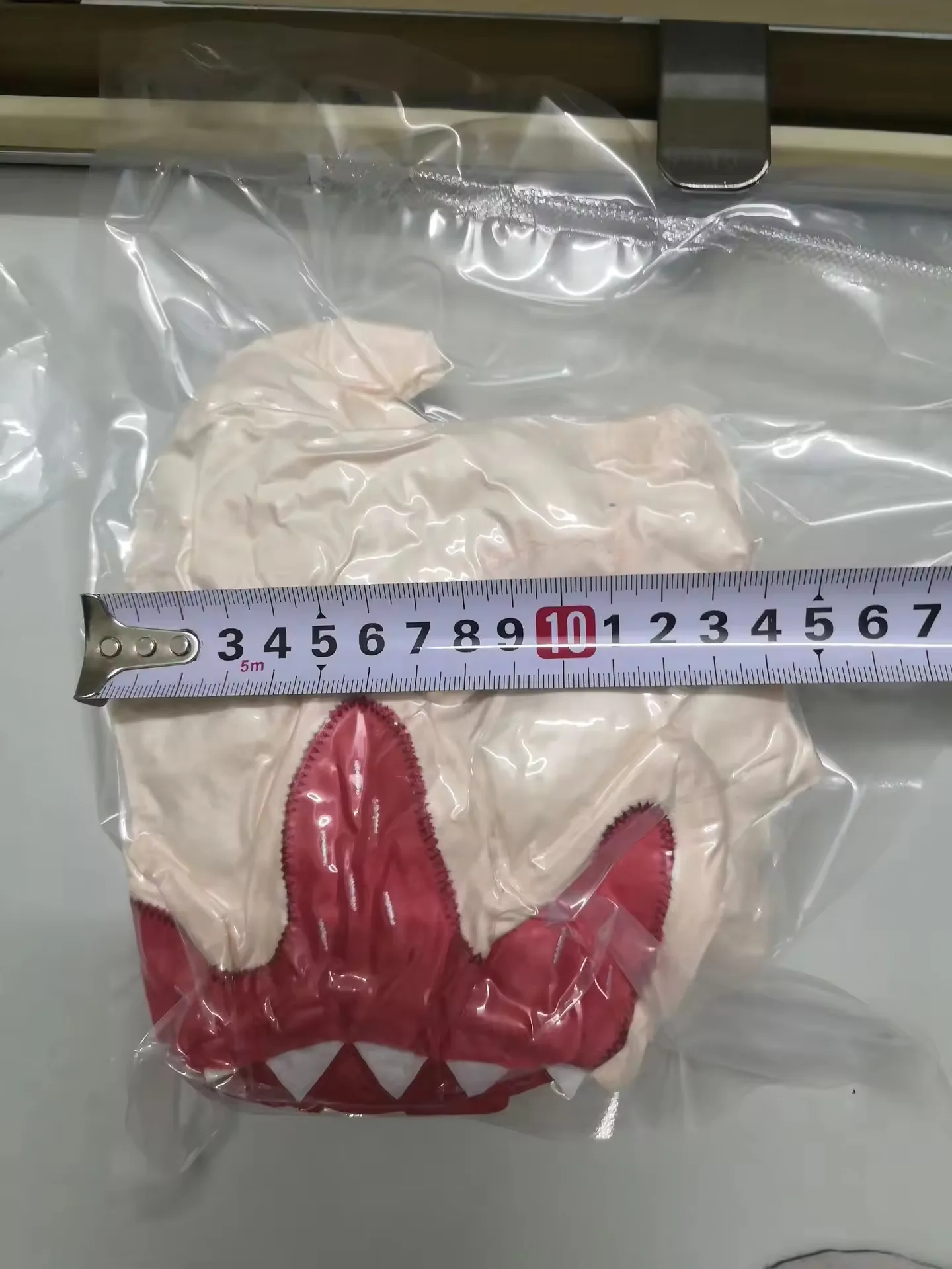 Peluche monstruo beige envasado al vacío junto a una regla para indicar el tamaño compacto del paquete