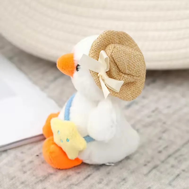 Detalle lateral del charm de peluche de pato blanco que muestra un sombrero de paja con lazo de cinta
