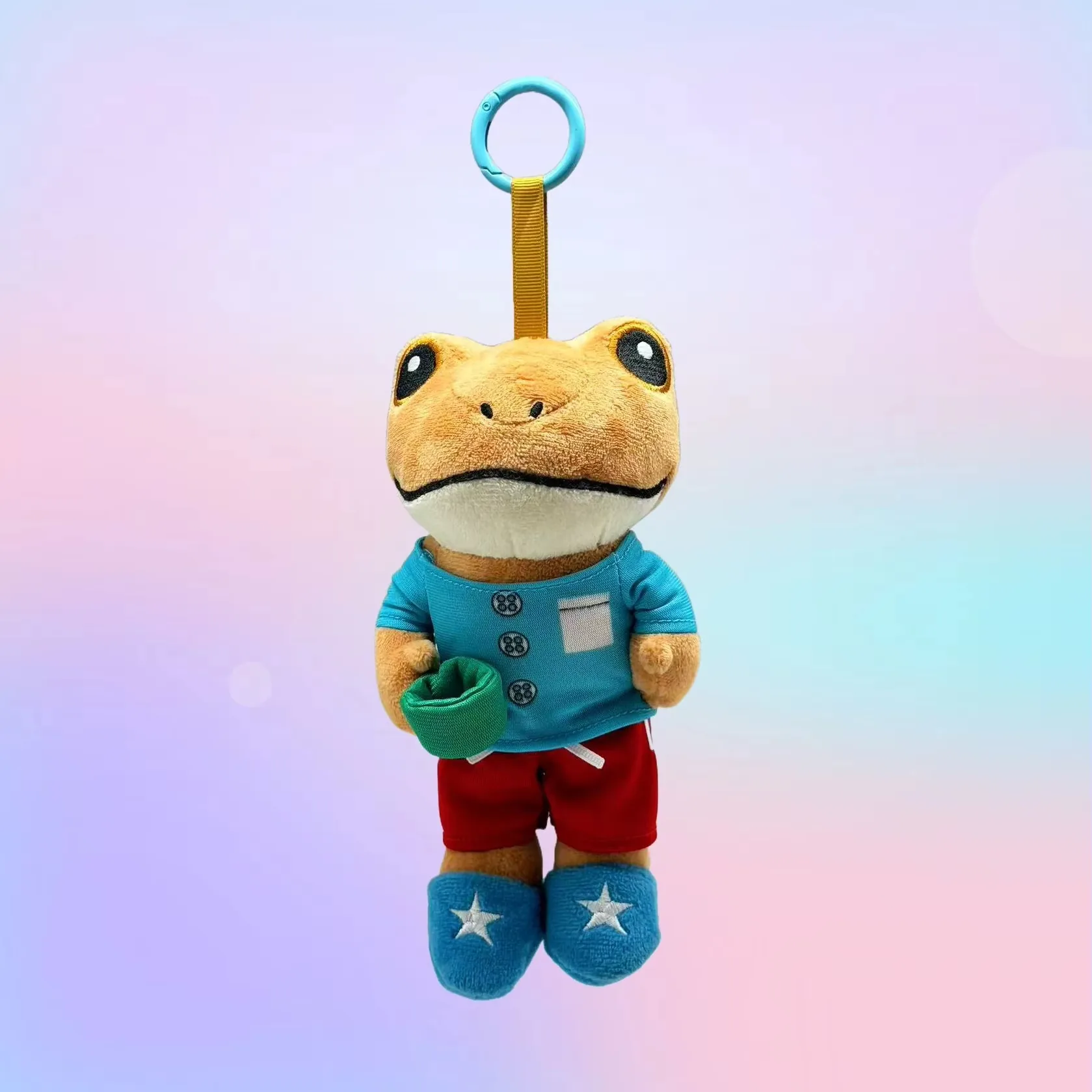 Llavero de rana de peluche con camiseta azul, shorts rojos y zapatos azules con detalles de estrella