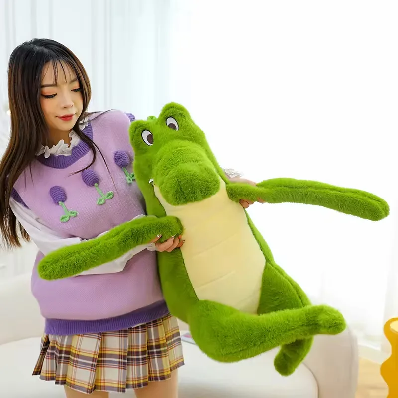 Una persona sosteniendo un peluche grande de cocodrilo verde para mostrar la escala del cuerpo y las extremidades largas y suaves