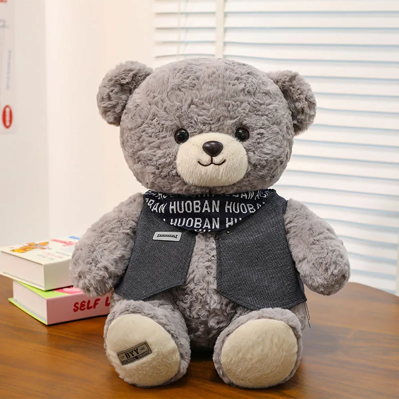 Peluche de oso teddy gris sentado de frente con pelo rizado, almohadillas crema y chaleco oscuro