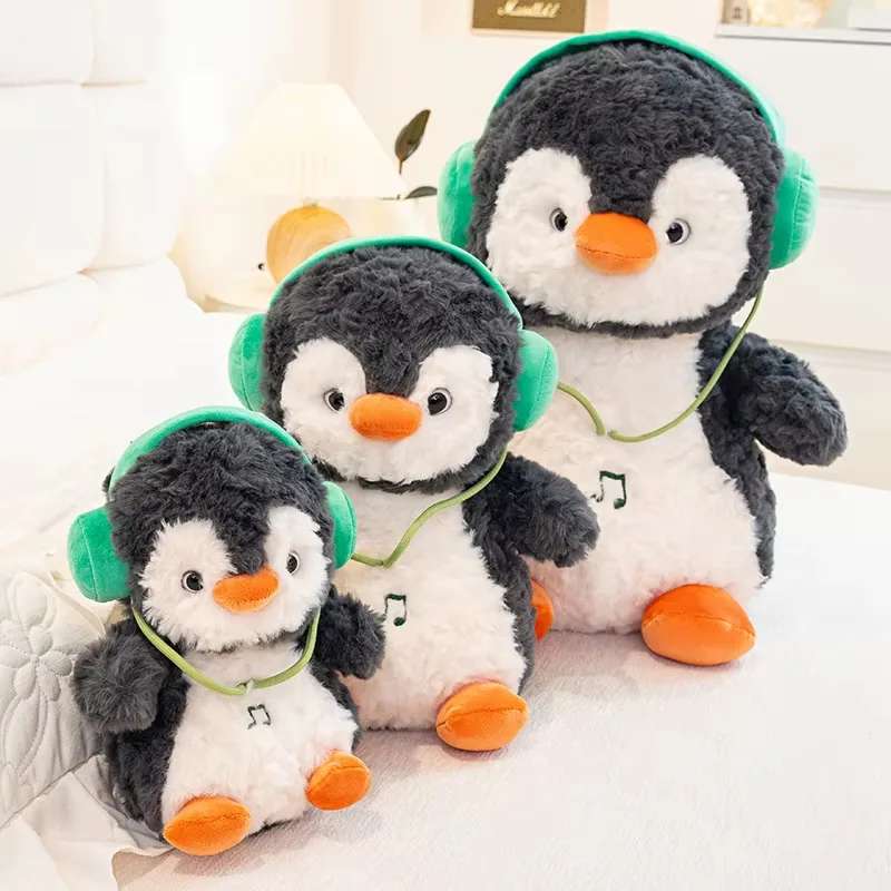 Tres muñecos de peluche de pingüino con auriculares colocados sobre una cama para mostrar la escala completa de pequeño a grande