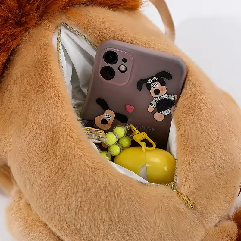 Compartimento de almacenamiento abierto dentro de la mochila de peluche de león con un teléfono y pequeños accesorios diarios