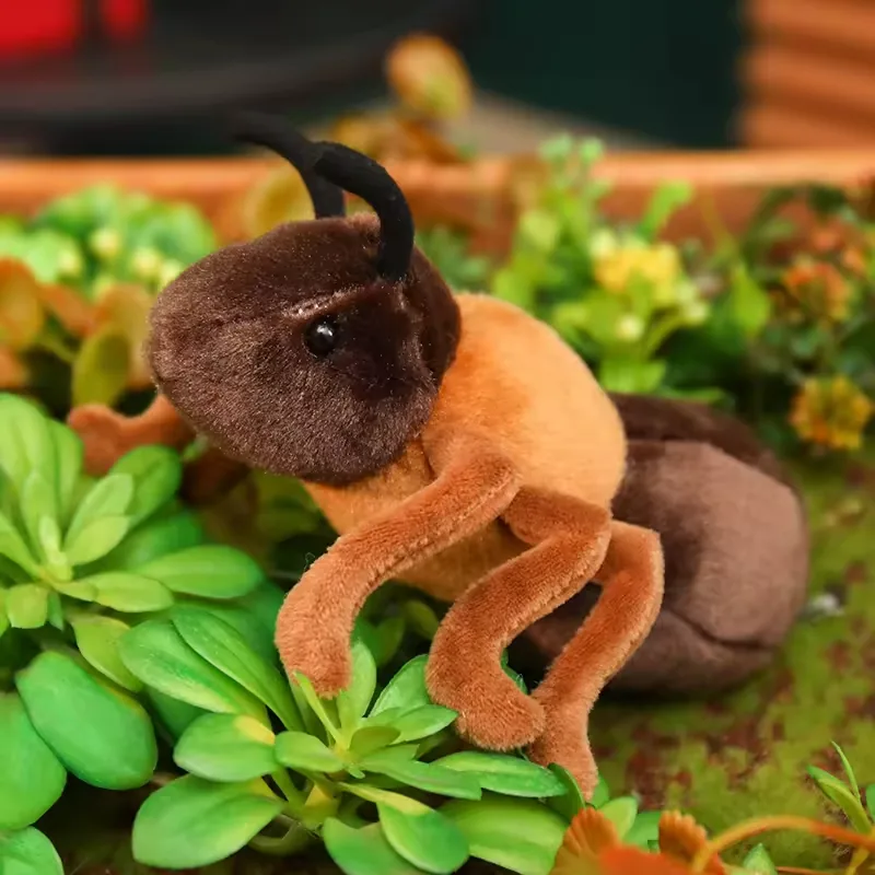 Peluche de hormiga realista posado entre plantas verdes con la cabeza levantada y patas suaves en postura de avance