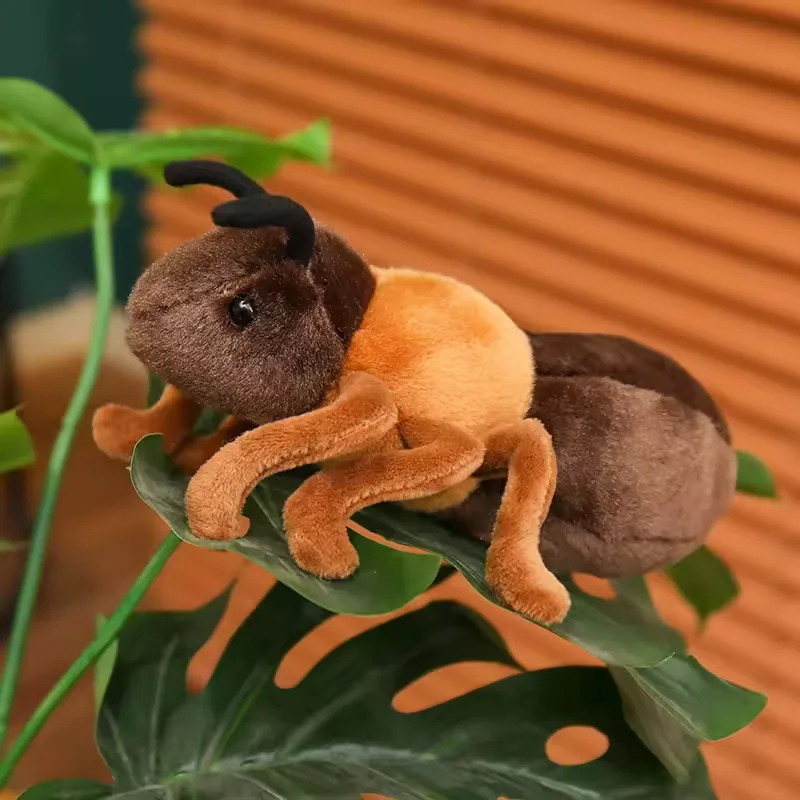 Peluche de hormiga realista apoyado sobre una hoja verde grande con cuerpo segmentado y antenas curvadas visibles