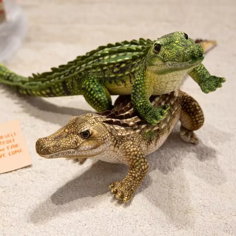 Peluches realistas de cocodrilo verde y marron claro apilados para comparar escala corporal, altura de la cresta y forma del hocico