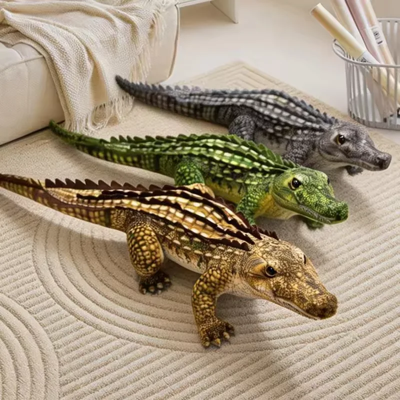 Peluches realistas de cocodrilo en gris, verde y marron claro colocados sobre una alfombra junto a un sofa para styling de regalo y hogar