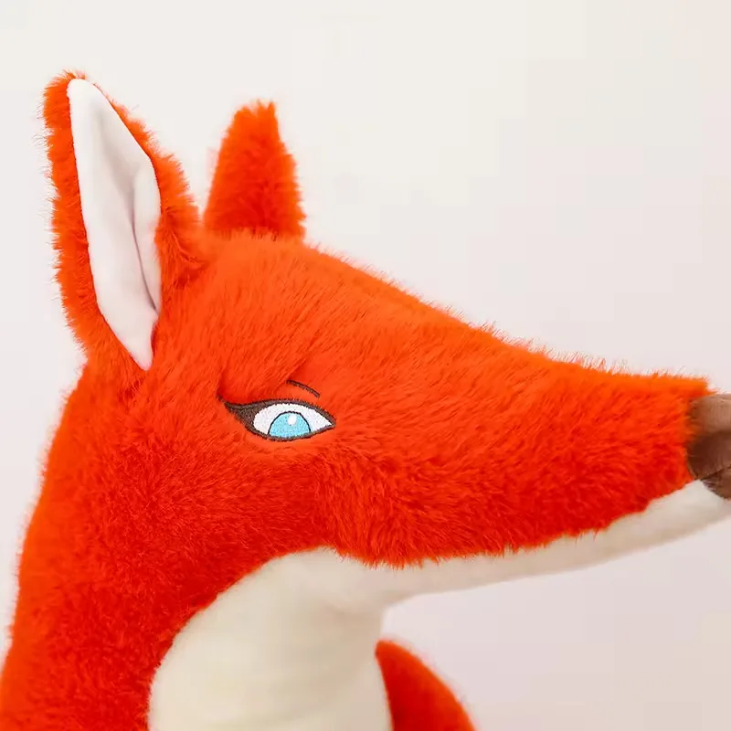 Primer plano de la cara del peluche de zorro rojo con ojo bordado azul, oreja erguida y nariz marron puntiaguda