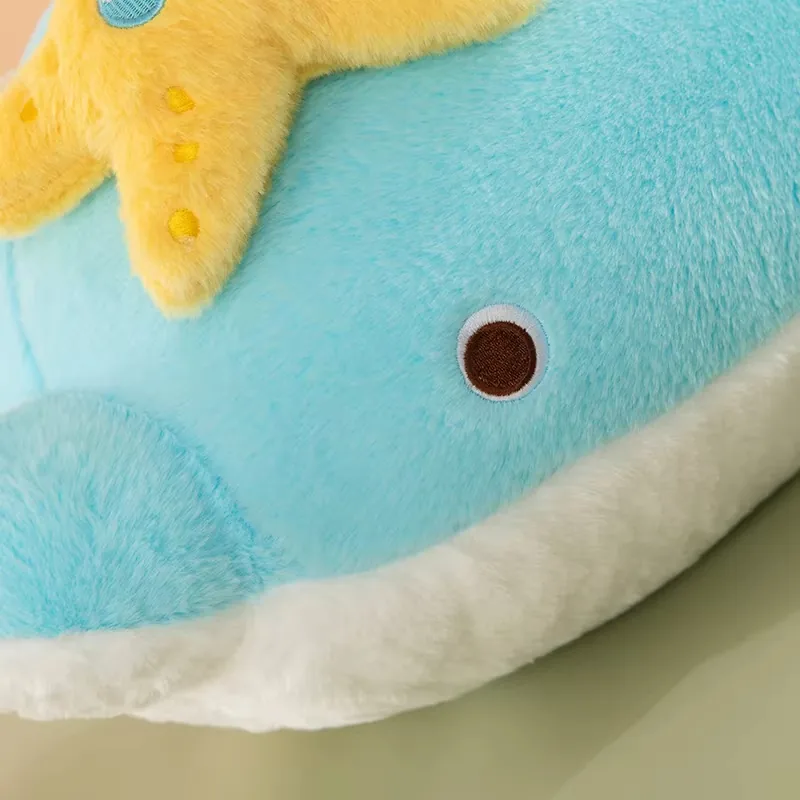 Primer plano del rostro del cojín de peluche de delfín azul con ojo bordado redondo y borde blanco en la barriga