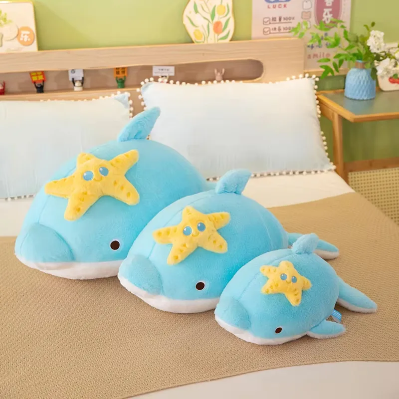 Tres cojines de peluche de delfín azules mostrados juntos en tamaños pequeño, mediano y grande sobre una cama