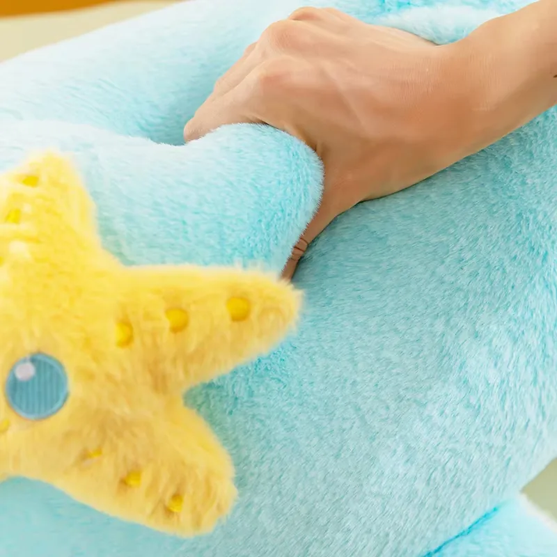 Una mano presiona el cojín de peluche de delfín azul para mostrar la textura suave y la capacidad de recuperación de la superficie