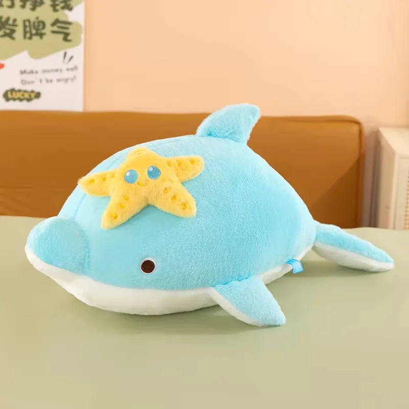 Cojín de peluche de delfín azul con panel blanco en la barriga y aplicación amarilla en la parte superior