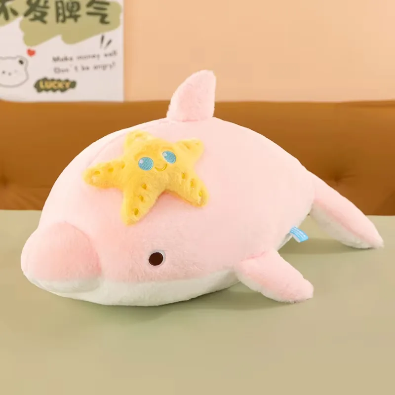 Cojín de peluche de delfín rosa con cuerpo suave en tonos pastel y aplicación de estrella de mar amarilla sonriente