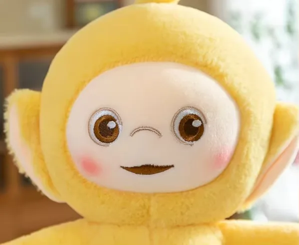 Primer plano del rostro del peluche amarillo Teletubbies con ojos bordados, mejillas rosadas y sonrisa tranquila