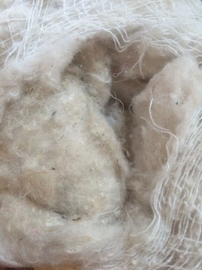 灰色がかった色味、密な塊、目に見える異物を含む低グレードぬいぐるみ充填材の接写