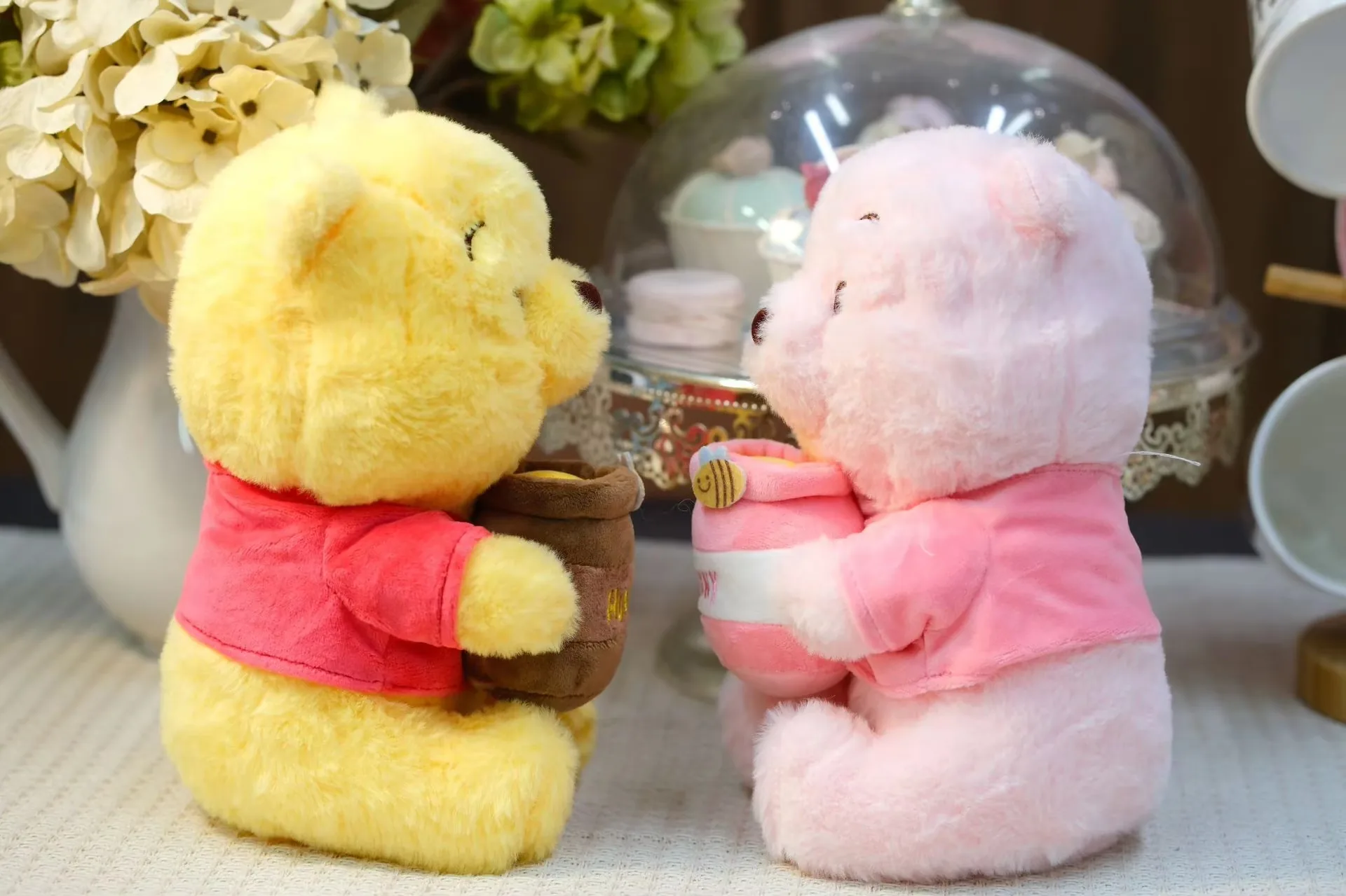 Vista lateral de los muñecos de peluche osito con tarro de miel en amarillo y rosa sentados frente a frente