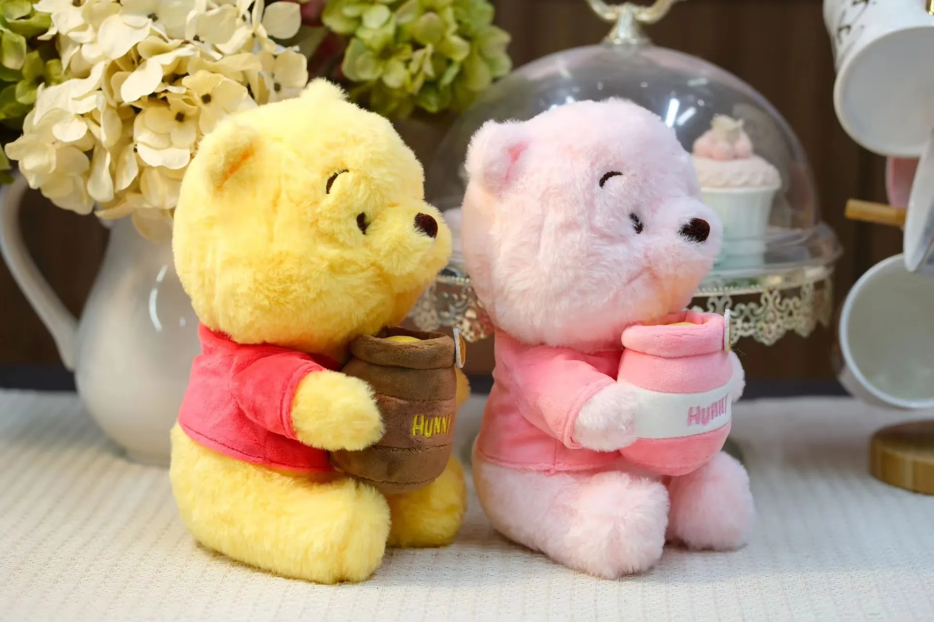Vista de tres cuartos de los muñecos de peluche osito con tarro de miel en amarillo y rosa mostrando el ángulo del tarro
